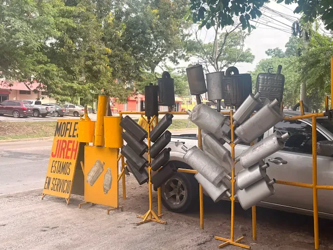 Mofles exhibidos en bases amarillas sobre la acera, con el rótulo Mofles Jireh Estamos en servicio